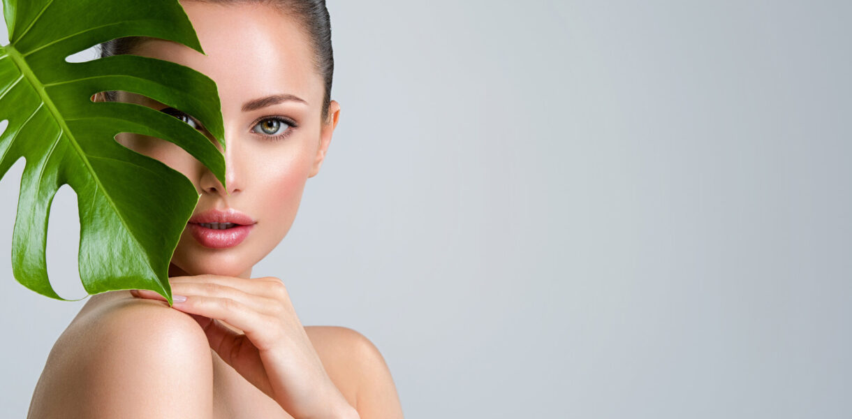 Junge schöne Frau mit grünen Blättern in der Nähe von Gesicht und Körper, Konzept der nachhaltigen Körperpflege für die Haut.