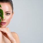Junge schöne Frau mit grünen Blättern in der Nähe von Gesicht und Körper, Konzept der nachhaltigen Körperpflege für die Haut.