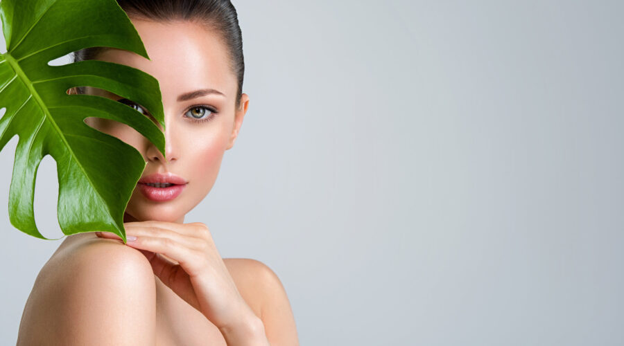 Junge schöne Frau mit grünen Blättern in der Nähe von Gesicht und Körper, Konzept der nachhaltigen Körperpflege für die Haut.