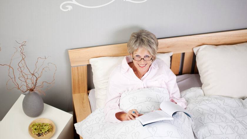 Seniorin liest entspannt und glücklich im Bett