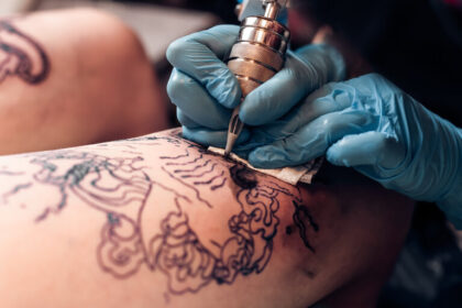 Closeup Tätowierer füllen Kreislauf Tattoo in einem professionellen Salon. Bein mit einem Muster und schwarzer Farbe. Meister arbeitet in schwarzen sterilen Handschuhen.
