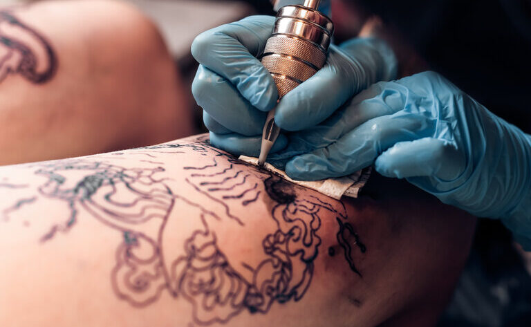 Closeup Tätowierer füllen Kreislauf Tattoo in einem professionellen Salon. Bein mit einem Muster und schwarzer Farbe. Meister arbeitet in schwarzen sterilen Handschuhen.